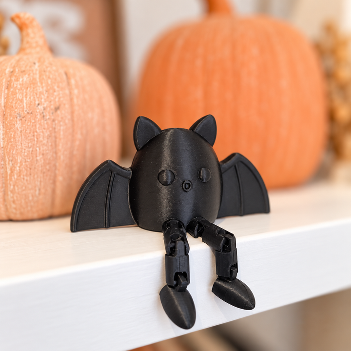 Black bat with dangling legs beside pumpkins