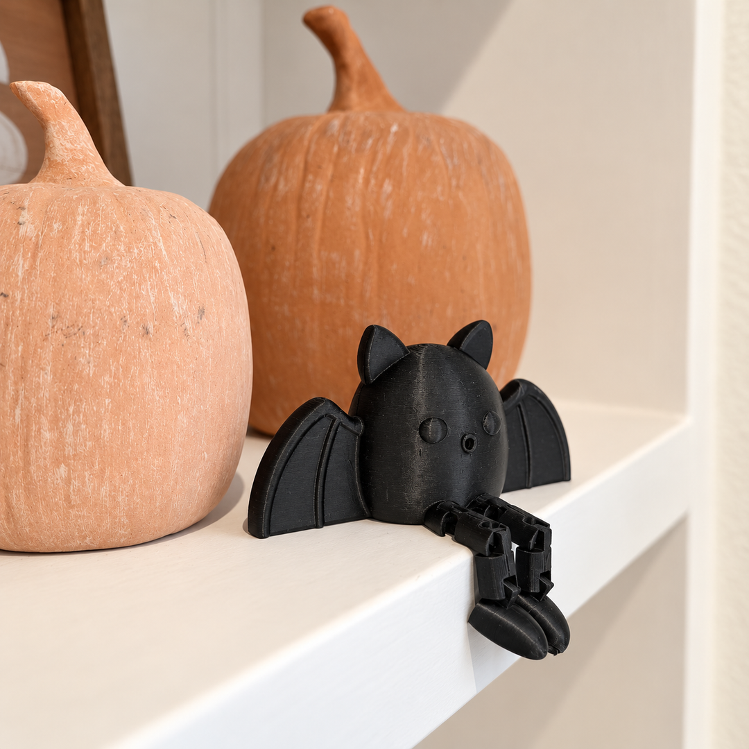 Black bat sitting on a shelf beside pumpkins