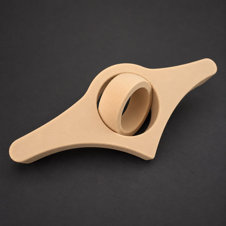 Light brown book page holder with its thumb ring tilted on a dark background